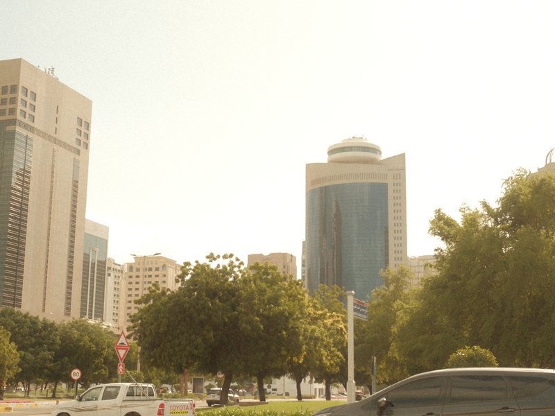 Cityscape featuring tall buildings and trees under a bright sky.