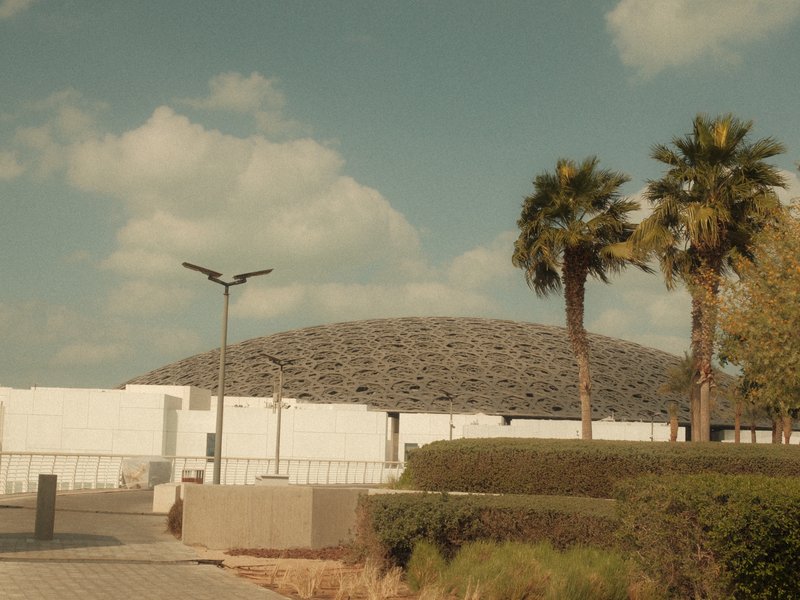 A modern architectural structure with a dome, surrounded by palm trees and a clear sky.
