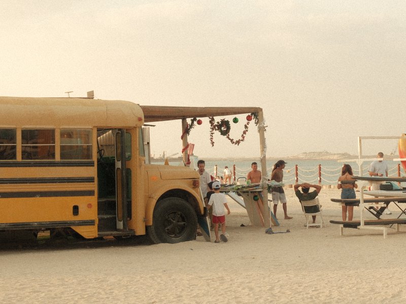 A yellow school bus converted into a beachside food stall with people enjoying the atmosphere.