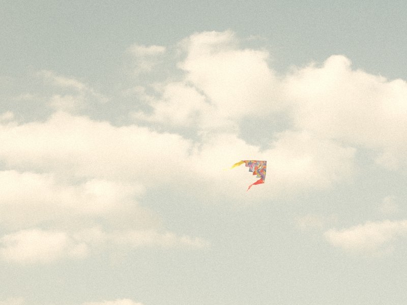 A colorful kite soaring in a light blue sky with fluffy white clouds.