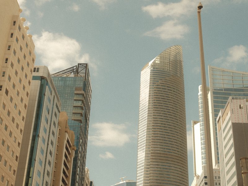 Skyscrapers reaching towards a blue sky with scattered clouds in an urban setting.