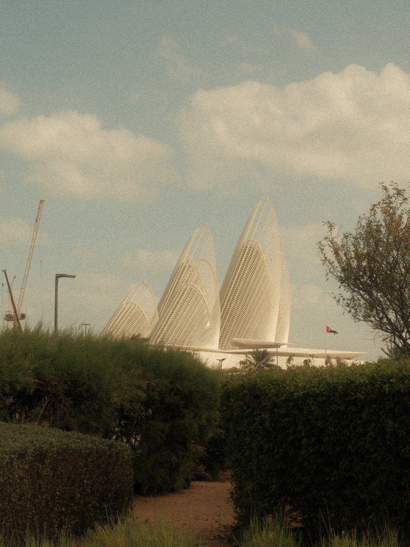 Three distinctive architectural structures partially obscured by greenery under a cloudy sky.
