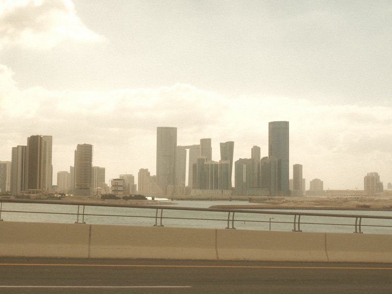 A hazy skyline of tall buildings along a waterfront, with a bridge in the foreground.