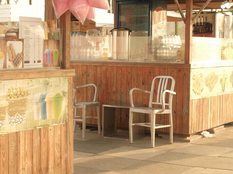 A wooden outdoor food stall with two empty chairs and colorful decorations.