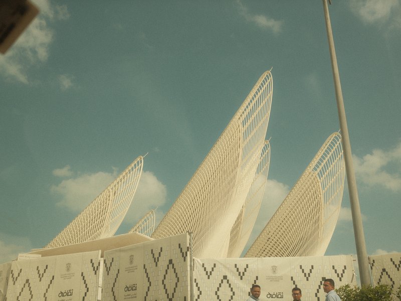 A modern architectural structure with pointed roofs against a blue sky and scattered clouds.