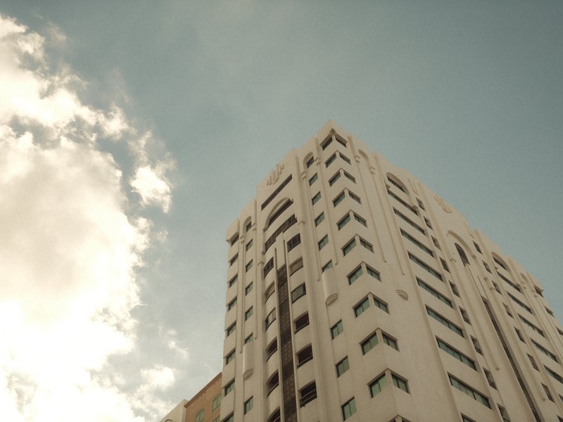 A tall modern building reaching towards a blue sky with scattered clouds.