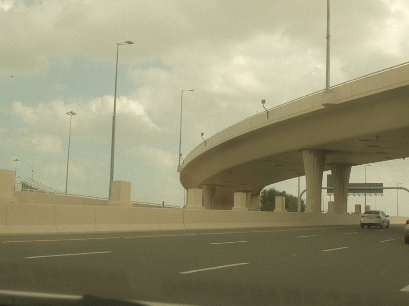 A highway overpass with a cloudy sky in the background, viewed from a moving vehicle.
