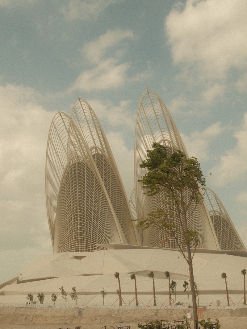 Modern architectural structure with unique curved designs under a cloudy sky, featuring a lone tree in the foreground.