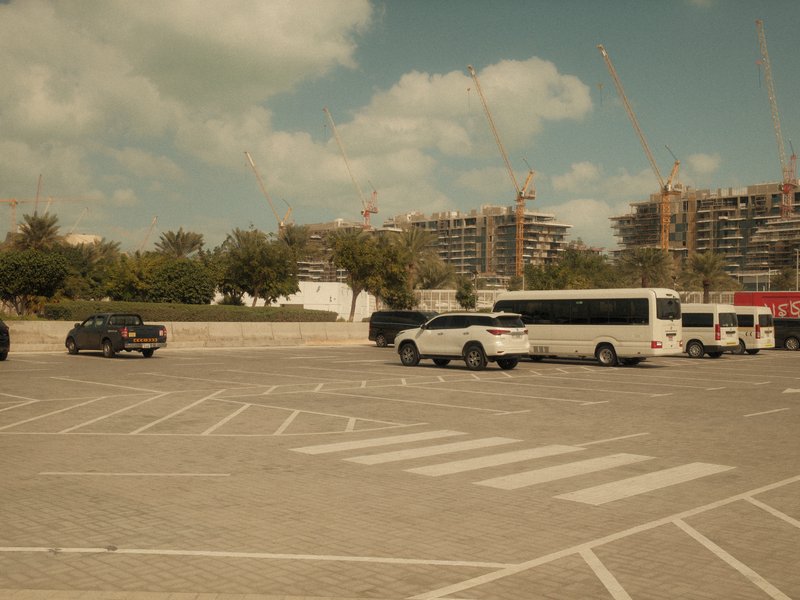 A parking lot with various vehicles, including buses and cars, set against a backdrop of construction buildings.