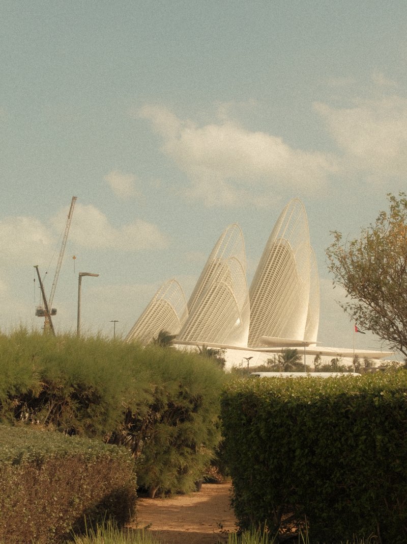 Three modern architectural structures rise above greenery under a cloudy sky.