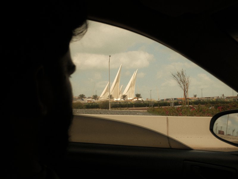 Silhouette of a person in a car with a modern architectural structure in the background.