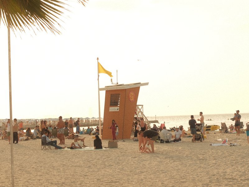 A beach scene with a lifeguard tower, people lounging on the sand, and a hazy sky.