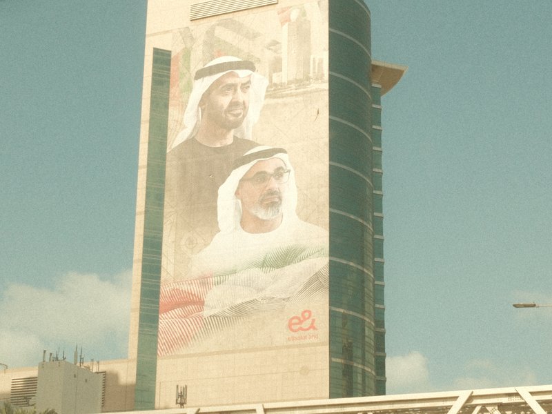 A large mural of two Emirati men on a tall building against a clear blue sky.