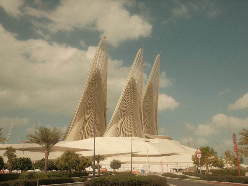 Modern architectural structure with three large, sail-like features against a blue sky with clouds.