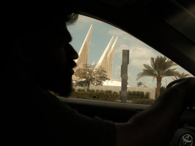 Silhouette of a person driving with a modern architectural structure and palm trees in the background.