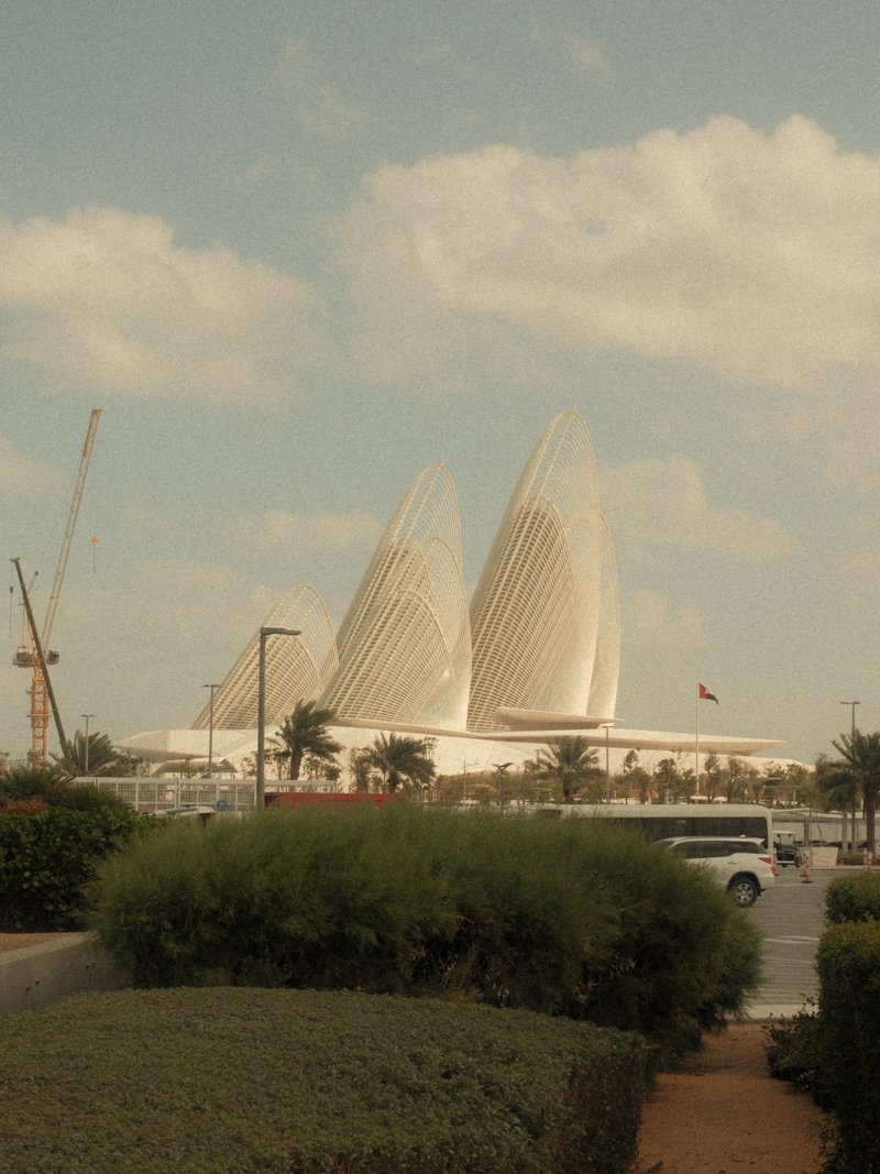 A modern architectural structure with three pointed towers against a cloudy sky, surrounded by greenery.