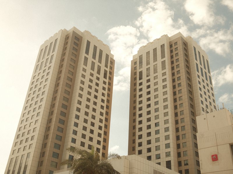 Two tall modern buildings under a bright sky with clouds, showcasing architectural design.