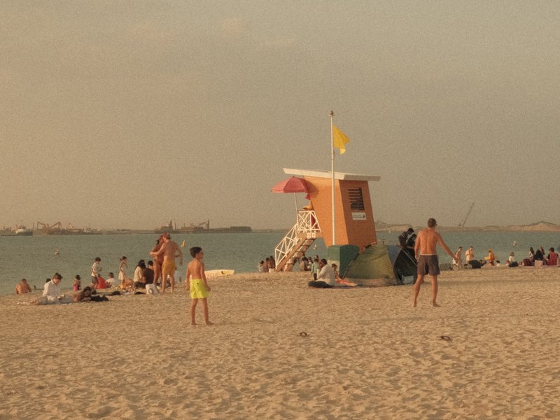 A beach scene with a lifeguard tower, people relaxing on the sand, and a calm sea in the background.