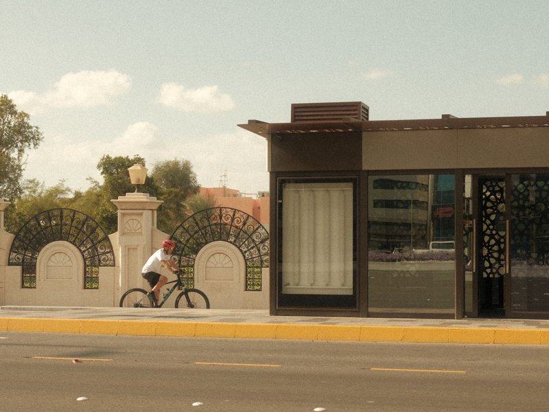 A cyclist rides past a modern building with decorative arches under a clear sky.