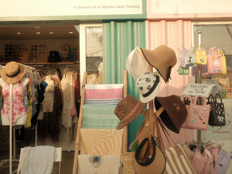 A colorful storefront displaying summer clothing and accessories, including hats and bags.
