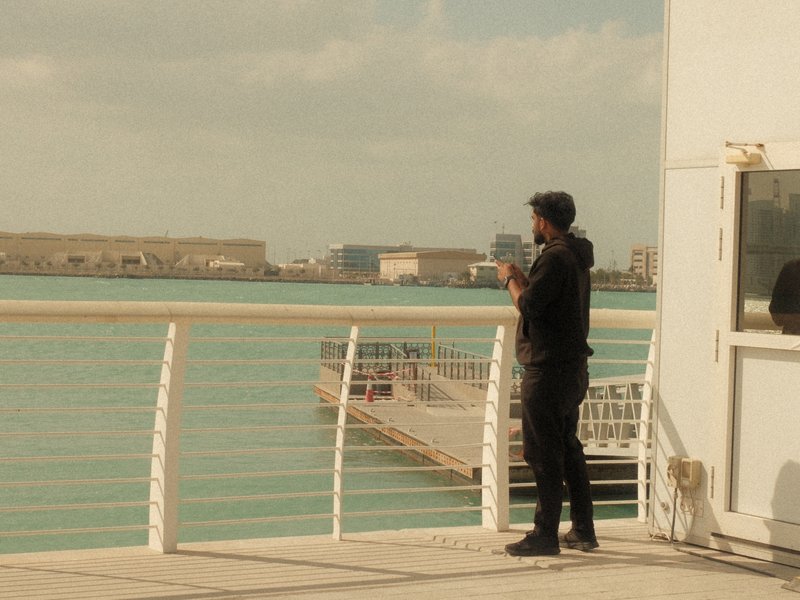 A person standing on a pier overlooking a turquoise body of water with a city skyline in the background.