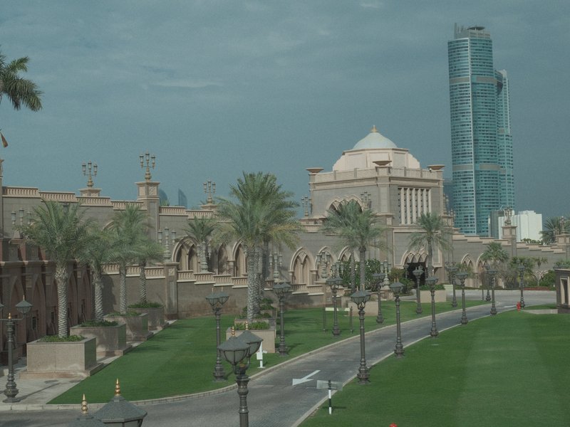 A view of a grand building with a dome, surrounded by palm trees and a modern skyscraper in the background.