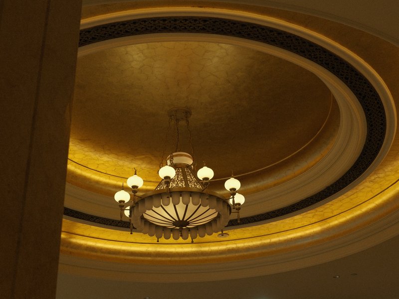 A decorative chandelier hanging from a golden ceiling with intricate patterns.