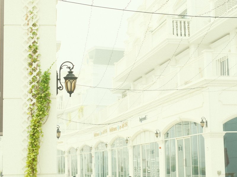 A soft, misty street scene featuring white buildings with decorative arches and hanging lanterns.