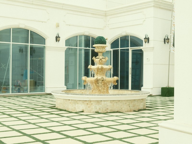 A decorative fountain in a courtyard with a tiled floor and large glass windows in the background.