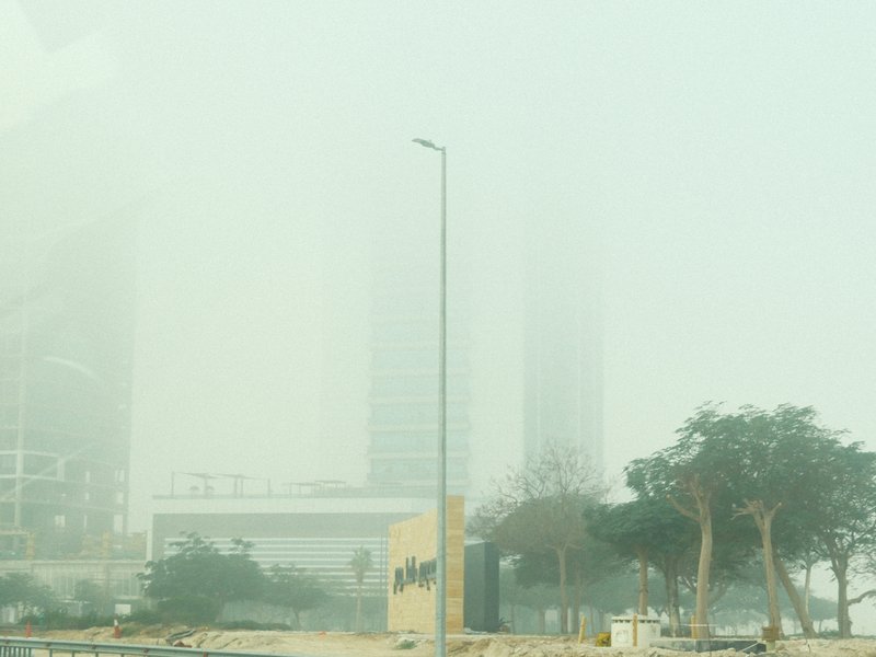 A foggy urban scene with a streetlight and blurred buildings in the background.