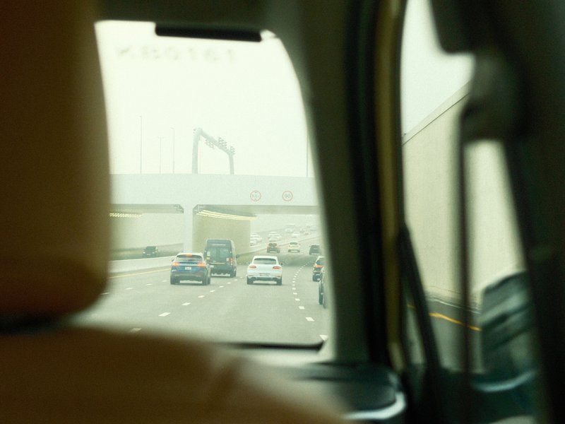 View from inside a car showing a busy highway with vehicles and a bridge in the background.