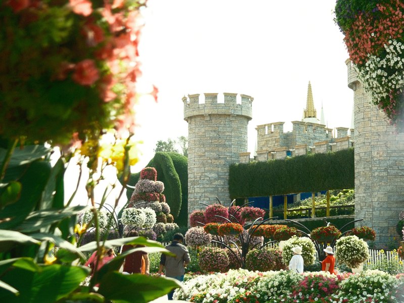 A vibrant garden scene featuring a castle backdrop surrounded by colorful flower arrangements.