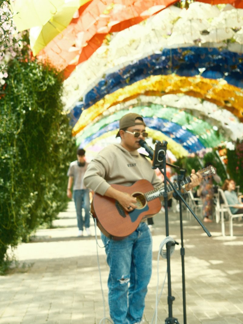 A musician playing guitar under a colorful canopy in a lively outdoor setting.
