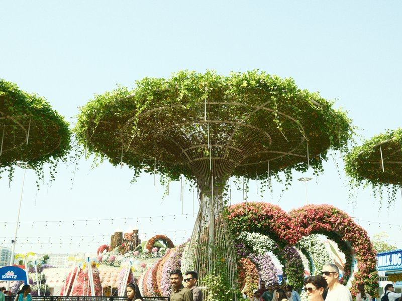 A large, tree-like structure adorned with greenery and flowers, surrounded by people at a festival.