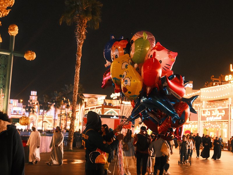 A person holding a large cluster of colorful balloons in a festive night market setting.