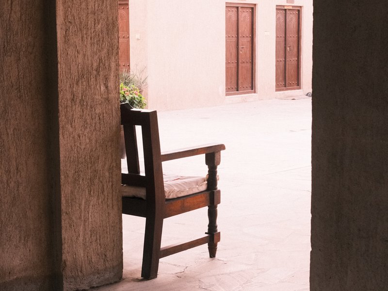 A wooden chair positioned in a quiet corridor with soft light and muted colors.
