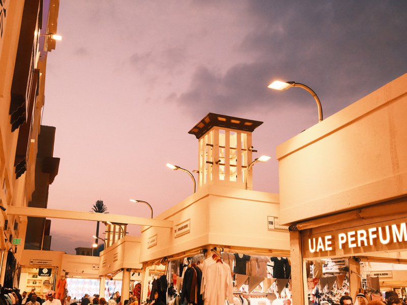 A bustling market scene at dusk with shops and a colorful sky.