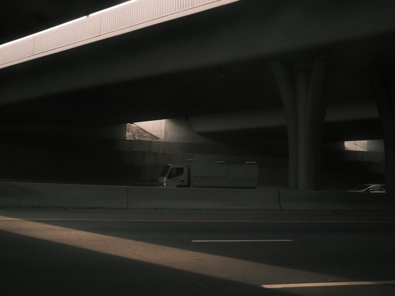 A truck parked under a highway overpass with soft light filtering through the structure.