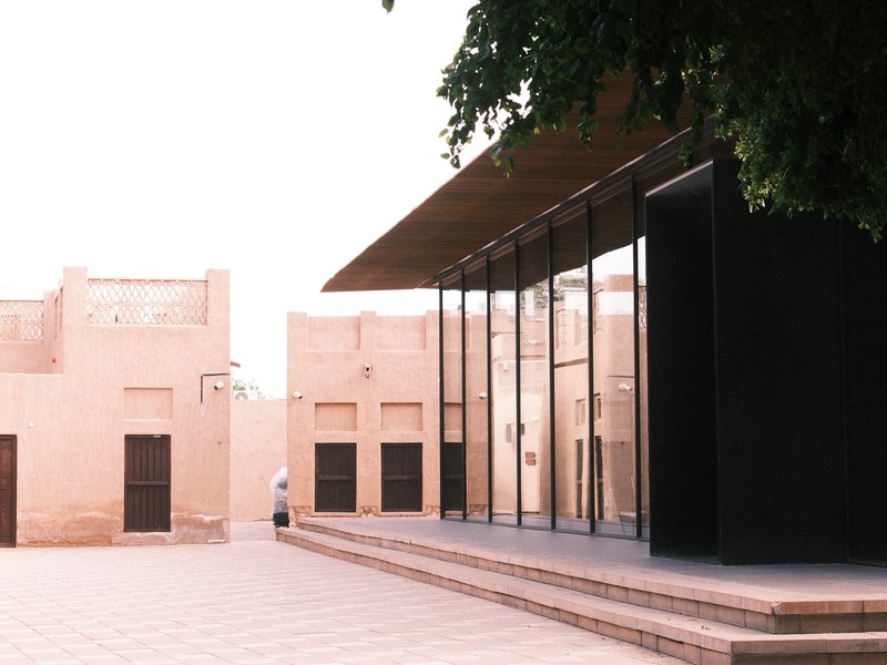 Modern glass building adjacent to traditional mud-brick structures in a courtyard setting.