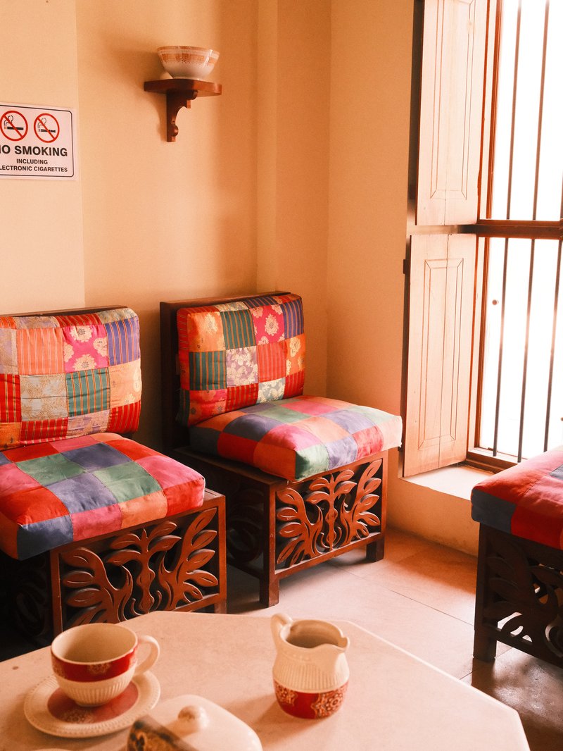 Colorful patchwork chairs in a cozy indoor setting with a small table and open window.