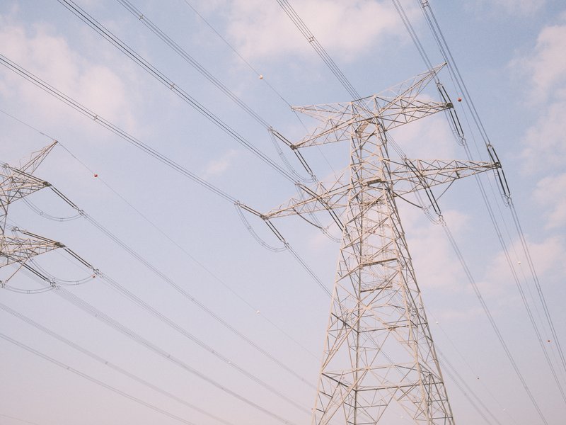 A tall electricity transmission tower against a pastel sky with power lines extending into the distance.