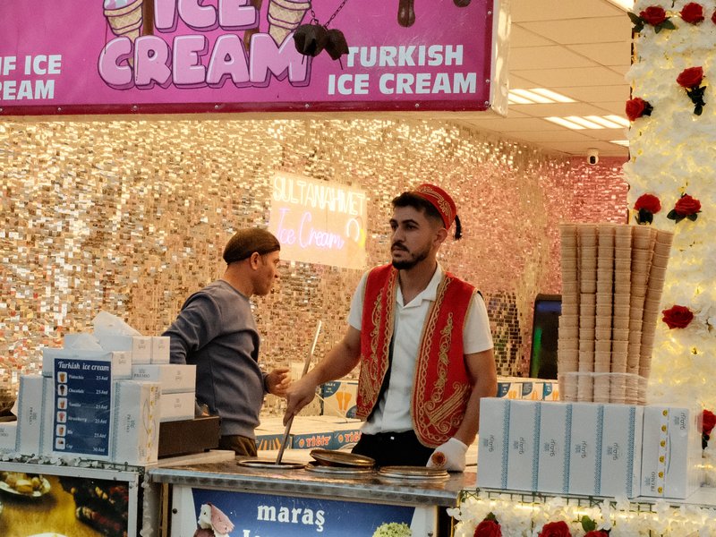 A vibrant ice cream stall with a vendor in traditional attire serving customers in a lively setting.