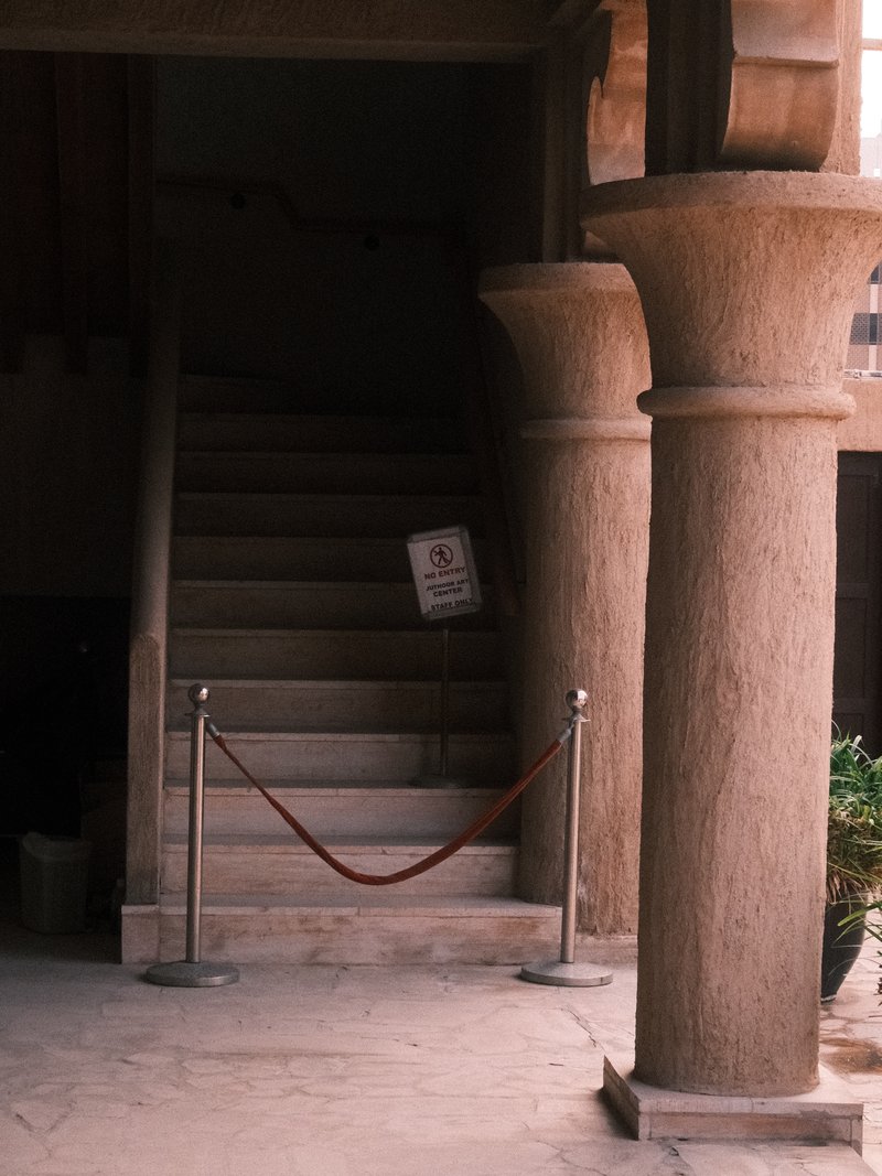 Interior view of a staircase with stone columns and a velvet rope barrier.