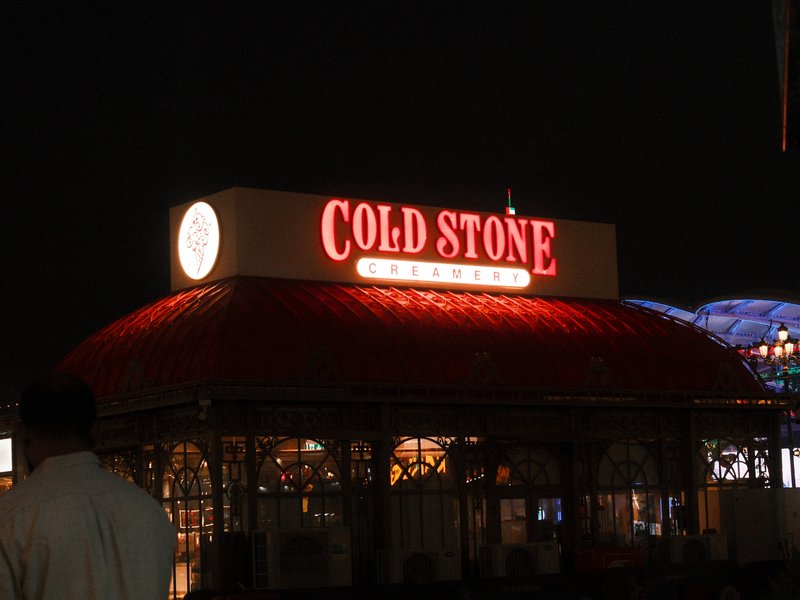 A brightly lit Cold Stone Creamery sign at night, with a red roof and surrounding urban atmosphere.