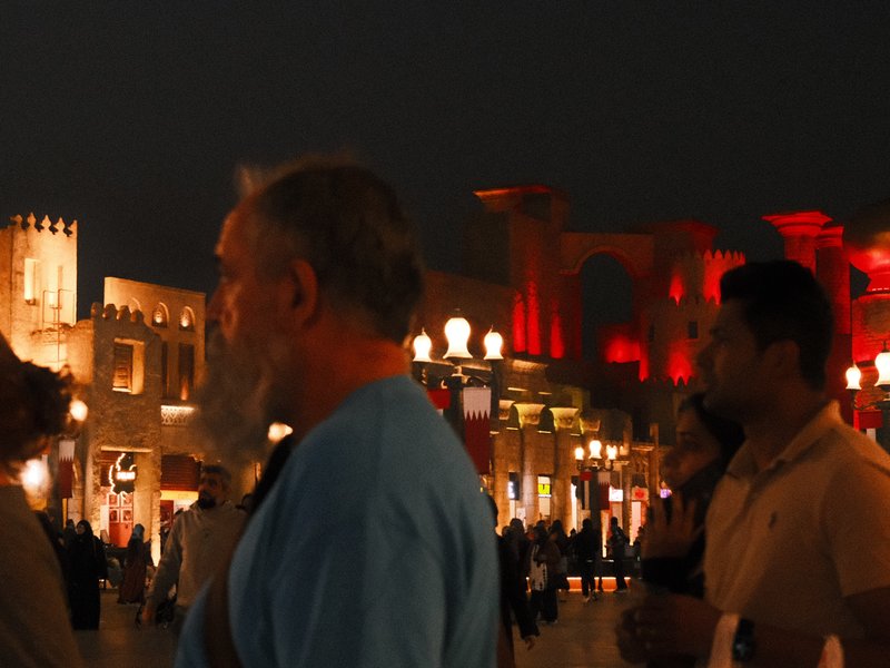 A crowd of people in a vibrant urban setting at night, with illuminated buildings in the background.