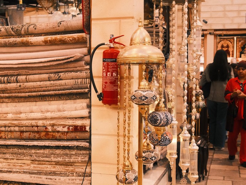 A vibrant market scene featuring decorative items, carpets, and a fire extinguisher.