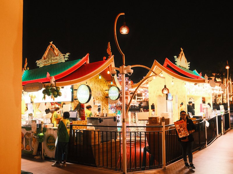 Vibrant night scene of a food market with colorful tents and people at stalls under warm lights.
