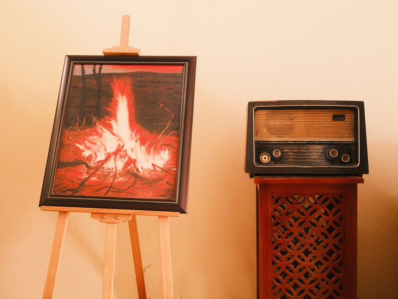 A framed picture of a campfire next to a vintage radio on a wooden stand.