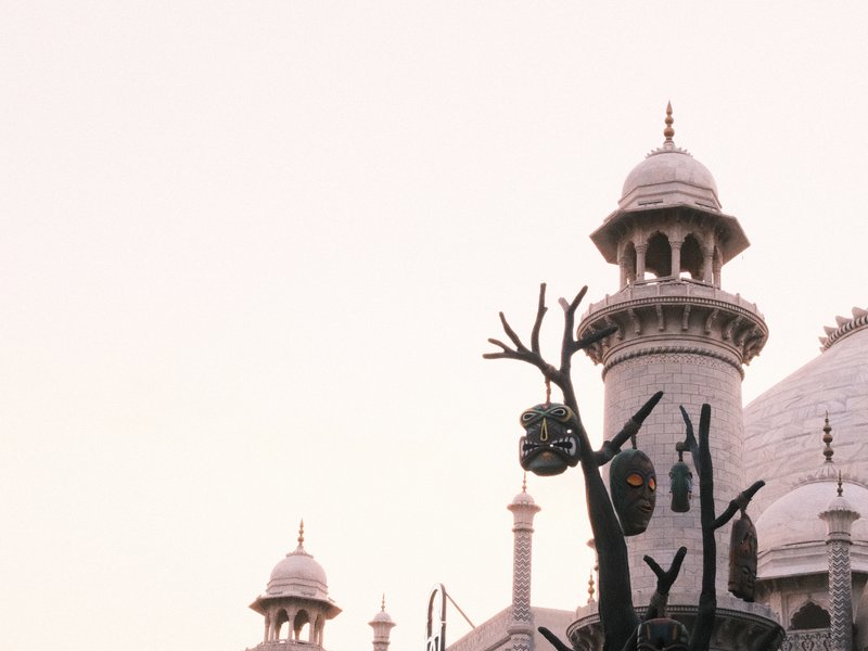 A close-up of a decorative tree with masks in front of a grand building with domes and spires.
