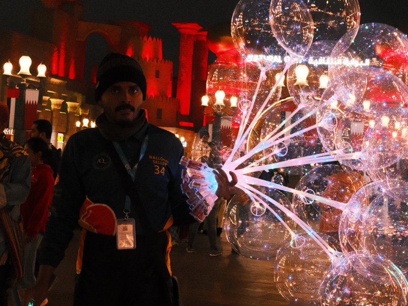 A street vendor holding illuminated bubbles in a festive urban setting at night.